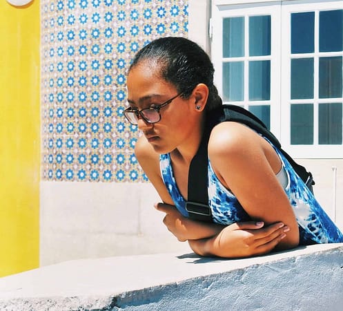 Young Cape Verdean woman observing passers-by in a typical Lisbon street whose facades are covered with tiles or azulejos.